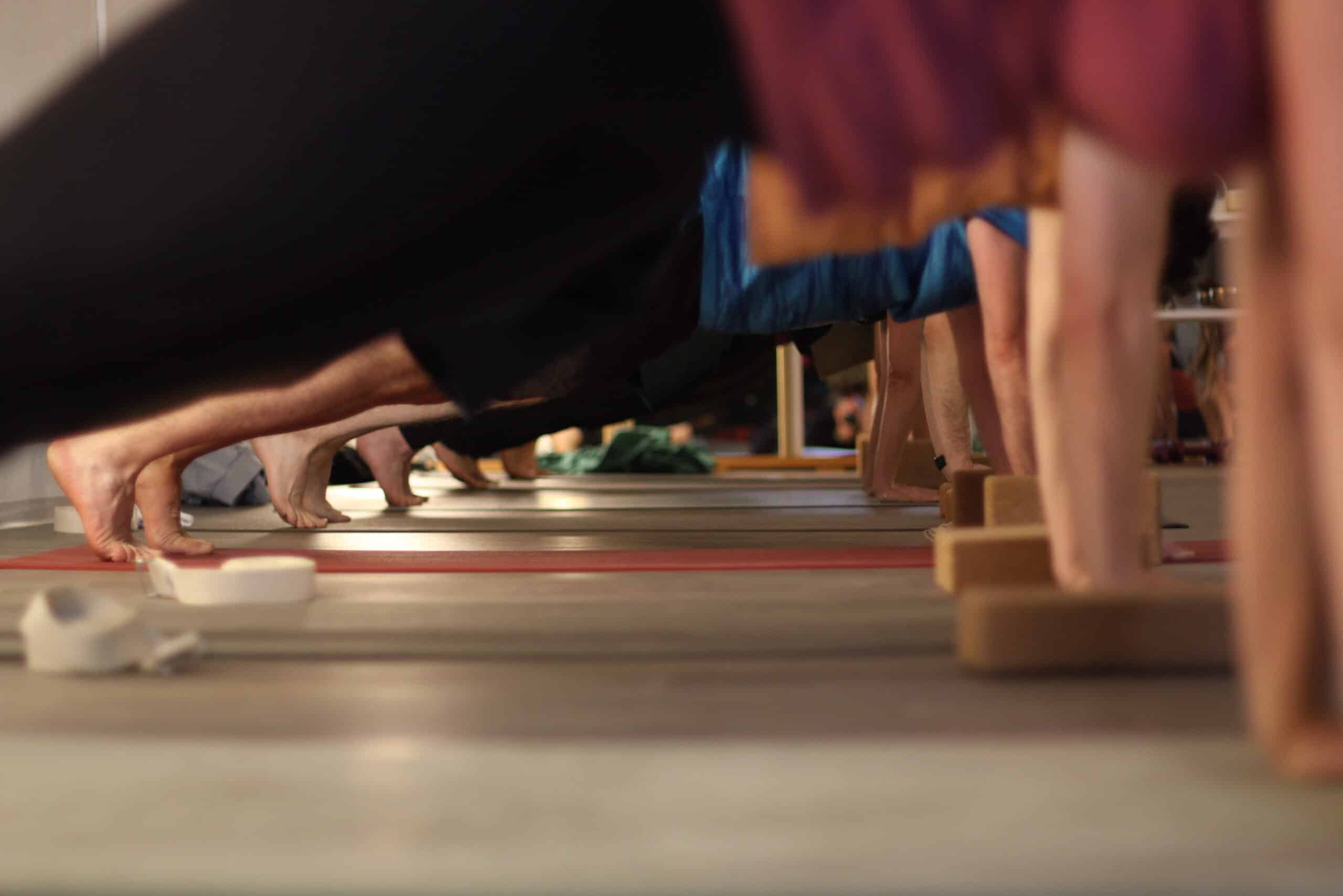 Participants en cours de yoga tenant une posture de planche. Vue de bas sur les pieds nus, les tapis et les blocs de bois de soutien.