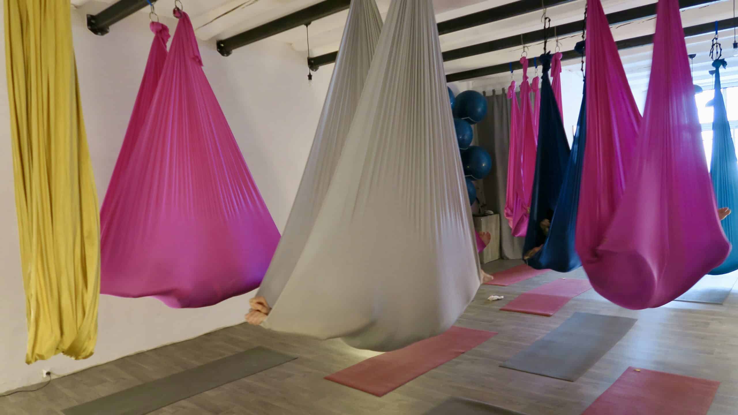 Cours de yoga aérien. Hamacs suspendus fuchsia, gris et bleu. Les participants se détendent dans les soies au-dessus des tapis de fitness.