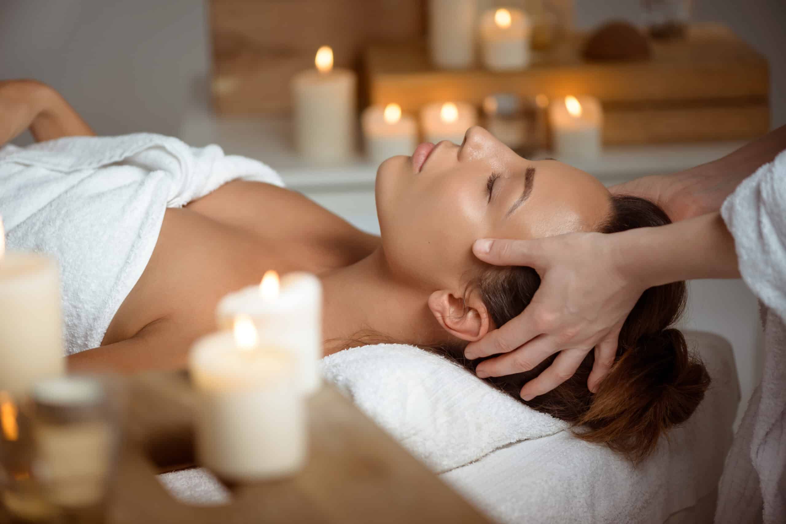 Massage relaxant du visage pour une femme, ambiance spa douce et bien-être avec de nombreuses bougies allumées.